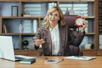 Mature businesswoman with alarm clock displaying time management in modern office