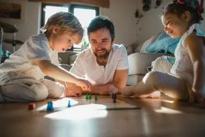 Mature father with two small children resting indoors at home, playing board games